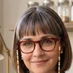 Margo Tally: bob haircut, red-framed glasses on a beaded chain, navy blazer over a striped top.